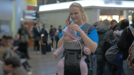 Mother-with-baby-daughter-waiting-at-the-airport-woman-talking-on-mobile