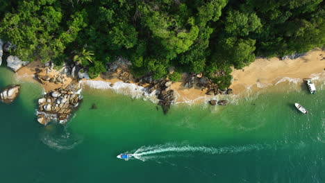 Aerial-view-above-a-boat-driving-on-the-coast-of-tropical-rainforest-and-jungle
