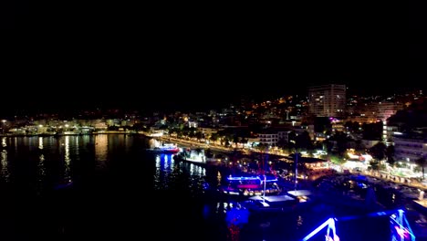 Night-Harbor-Elegance:-Leisure-Tour-Ships-Gracefully-Anchored-on-Saranda's-Coastal-Pier,-Illuminated-by-Neon-Lights,-Creating-a-Mesmerizing-Scene