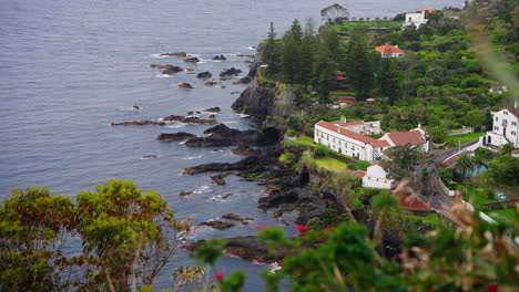 High-view-of-local-town-located-on-top-of-rocky-coastline-surrounded-by-green-lush-vegetation