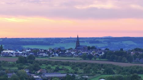 Across-village-landscape-dominated-by-imposing-church-spire,-sunset-scene