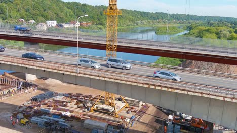 Semi-trucks-and-cars-crossing-bridge-near-construction-site,-aerial-drone-view