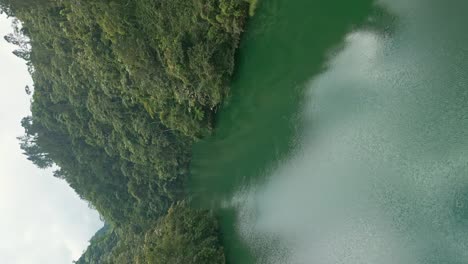 Aerial-vertical-flight-over-Tireo-Dam-with-green-river-water-and-tropical-rainforest-landscape-in-Bonao