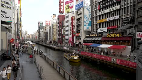 Blick-Auf-Den-Dotonbori-Kanal-Mit-Dem-Tombori-Flusskreuzfahrtschiff,-Das-An-Einem-Bewölkten-Tag-In-Osaka-Entlangfährt
