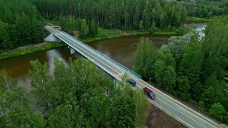 Drone-flight-over-a-river-car-bridge-in-the-middle-of-a-large,-green-forest