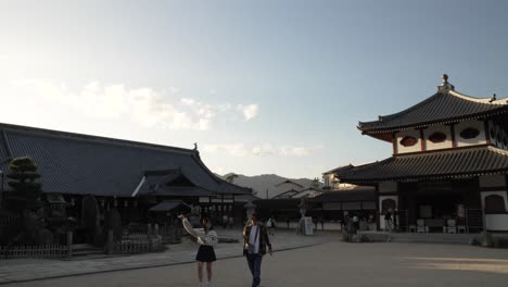 Daiganji-And-Gomado-Temple-On-Miyajima-Island-Back-lit-By-Sunset-Lit-And-Tourists-Walking-Past