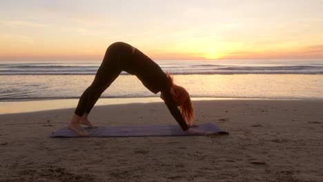 Frau-Am-Strand,-Die-Hundepose-Vorführt-Und-Bei-Sonnenaufgang-Yoga-Praktiziert