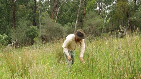 Ein-Historisch-Aussehender-Australischer-Buschmann-Schneidet-Gras-Auf-Einem-Feld-In-Der-Nähe-Des-Busches