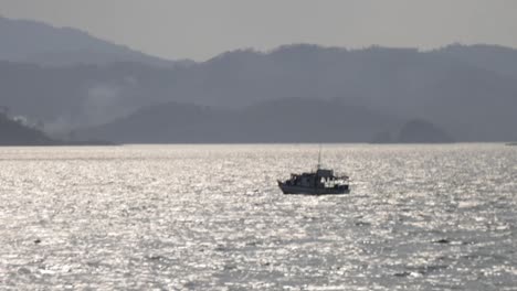Ein-Fischerboot,-Das-Im-Meer-In-Einer-Halbinselähnlichen-Landschaft-Mit-Bergen-Und-Einer-Küste-Im-Hintergrund-Segelt