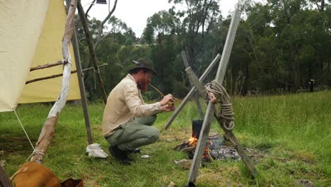 Australian-bushman-by-his-historical-camp-lights-up-a-tobacco-pipe-by-a-campfire-in-the-bush