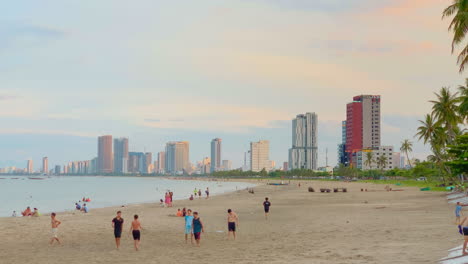 Strandszene-Bei-Sonnenuntergang,-Menschen,-Die-Mit-Hotels-Spielen-Und-Spazieren-Gehen,-Hochhäuser-Im-Hintergrund