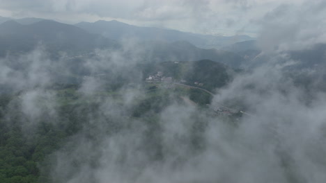 Aerial-view-through-fog,-revealing-a-town-in-th-Shiga-Kogen-mountains,-in-Japan