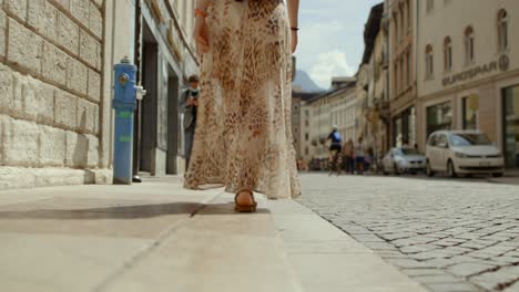 Low-Angle-Shot-Of-Solo-Female-Traveller-Wearing-Summer-Dress-Walking-Along-European-Street-On-Sunny-Day