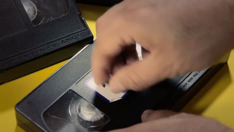 Applying-a-white-label-on-a-VHS-tape,-with-the-handwritten-text-2000s