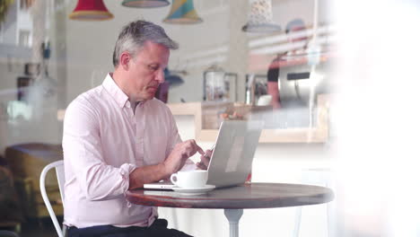 Businessman-with-a-laptop-at-a-table-in-a-cafe-using-phone