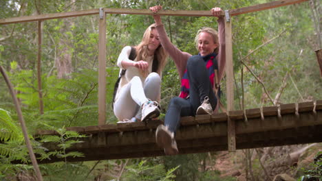 Mother-and-daughter-sitting-on-a-small-bridge-in-a-forest