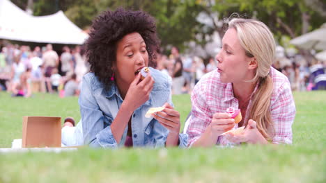 Two-friends-lying-on-the-grass-and-eating-cakes-at-an-event