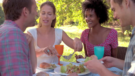 Four-friends-eating-at-a-table-together-outdoors