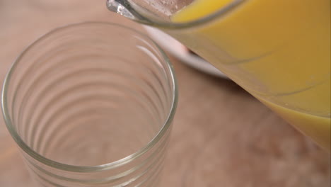 Slow-Motion-Shot-Of-Pouring-Orange-Juice-Into-Glass-From-Jug