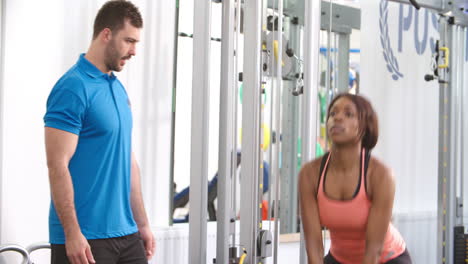 Frau,-Die-Mit-Einem-Trainer-In-Einem-Fitnessstudio-Ein-Kettlebell-Gewicht-Benutzt