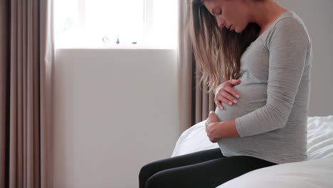 Mujer-Embarazada-Deprimida-Sentada-En-La-Cama-Sosteniendo-El-Vientre