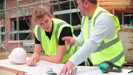Builder-On-Building-Site-Discussing-Work-With-Apprentice