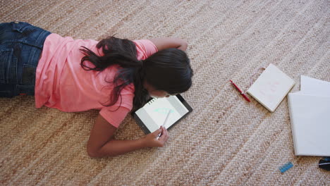 Teenager-Mädchen-Liegt-Im-Wohnzimmer-Auf-Dem-Boden-Und-Benutzt-Einen-Tablet-Computer-Und-Einen-Stift,-Blick-Von-Oben