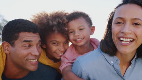 African-American-parents-piggybacking-their-kids-in-the-garden,-looking-to-camera-and-laughing,-close-up
