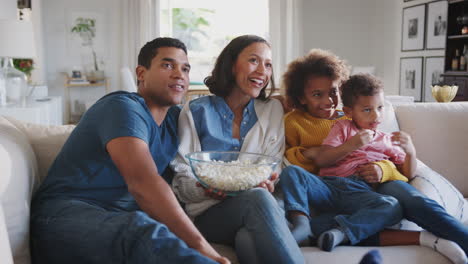 Young-African-American-family-sitting-on-the-sofa-at-home-watching-TV-and-eating-popcorn