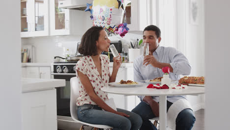 Junges-Paar-Sitzt-Am-Tisch-In-Der-Küche-Und-Stößt-An,-Bevor-Es-Gemeinsam-Ein-Romantisches-Essen-Zu-Sich-Nimmt