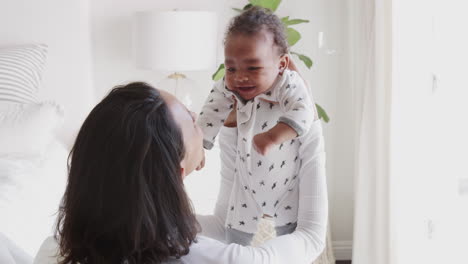 Millennial-African-American-mother-lifting-her-baby-and-smiling-at-him,-over-shoulder-view