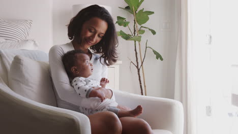Happy-millennial-African-American-mother-sitting-in-rocking-chair-holding-her-baby