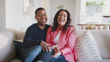 Middle-aged-African-American-couple-embracing-on-the-sofa-in-their-living-room-laughing,-close-up