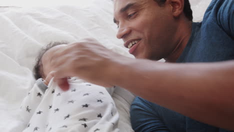 Close-of-millennial-African-American-father-lying-on-the-bed-playing-with-his-baby-son