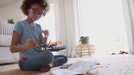 Pre-teen-African-American-girl-sitting-on-the-floor-building-a-construction-kit-toy,-close-up,-full-length