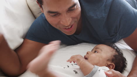 Close-of-millennial-African-American-father-lying-on-bed-playing-with-his-newborn-baby-son