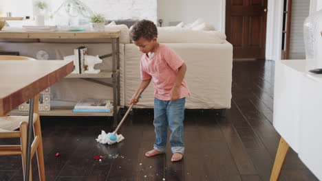 Three-year-old-African-American-boy-cleaning-dining-room-floor-with-a-mop,-full-length