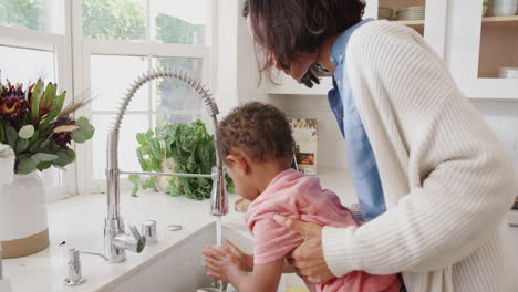Millennial-mum-standing-at-the-kitchen-sink-helping-her-son-wash-his-hands,-side-view,-close-up