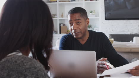Afroamerikanischer-Mann-Mittleren-Alters-Mit-Laptop,-Der-Einer-Frau-Zu-Hause-Finanzberatung-Gibt,-Aus-Nächster-Nähe