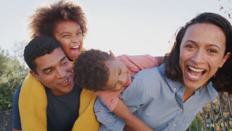Padres-Jóvenes-Afroamericanos-Y-Sus-Hijos-Divirtiéndose-En-El-Jardín-Mirando-A-La-Cámara,-De-Cerca