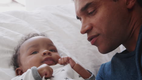 Close-of-millennial-African-American-father-lying-on-the-bed-kissing-his-baby-son