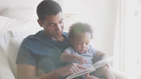 Millennial-African-American-father-sitting-and-reading-a-book-with-his-toddler-son,-front-view,-close-up