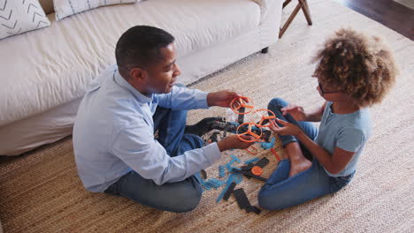 Pre-teen-African-American-girl-and-grandad-sitting-cross-legged-on-the-floor-constructing-a-toy,-elevated-view