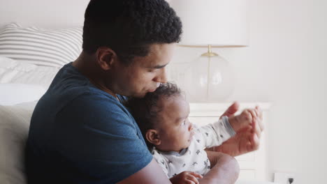 Millennial-African-American-dad-rocking-in-an-armchair-holding-his-baby-boy,-close-up,-side-view