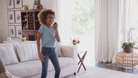 Pre-teen-African-American-girl-dancing-and-singing-at-home-using-phone-as-a-microphone,-three-quarter-length