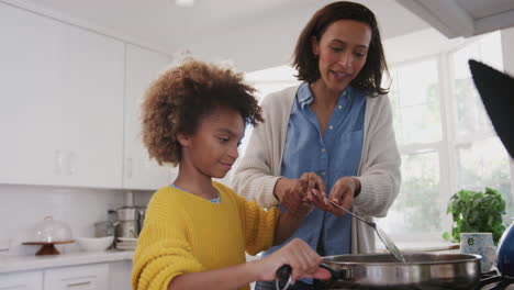 Mother-helping-her-pre-teen-daughter-cook-food-in-a-pan-at-the-hob-in-the-kitchen,close-up