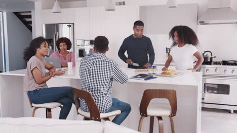 Happy-black-family-at-their-kitchen-island,-talking-and-preparing-a-family-meal-together