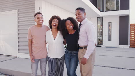 Black-family-stand-looking-to-camera-in-front-of-their-modern-home,-three-quarter-length