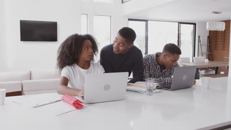 Middle-aged-black-dad-helping-his-teen-kids,-doing-their-homework-using-laptops,-front-view