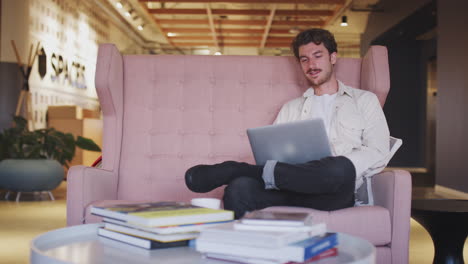 Millennial-weißer-Kreativer-Mann,-Der-Auf-Einem-Sofa-In-Einer-Bürolobby-Sitzt-Und-Einen-Laptop-Computer-Benutzt